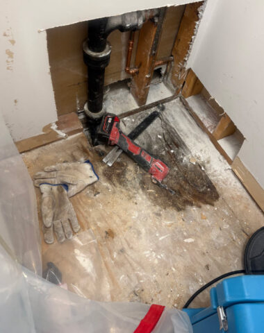 Open wall with exposed pipes shows water damage restoration work in progress